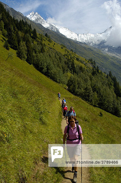 Hiking group one after another on a path crossing a grassy slope Haute-Savoie France