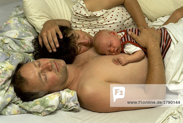 Eltern mit neugeborenem Baby liegen schlafend im Bett