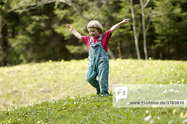 One three-year-old girl running down a meadow in spring
