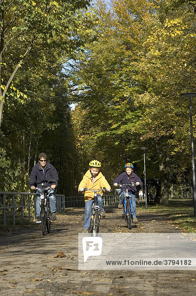 Mutter mit siebenjährigem und neunjährigem Sohn bei Radfahren am Isarradweg im Herbst in München