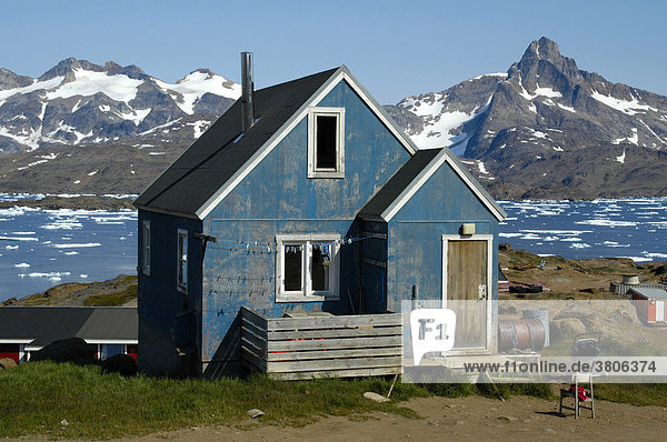 Altes Haus blau gestrichen vor Fjord vor Packeis und schneebedeckten Bergen Ammassalik Ostgrönland