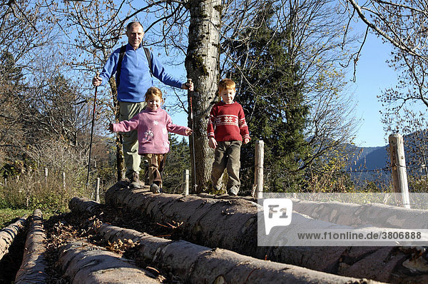Kinder balancieren mit ihrem Großvater auf Baumstämmen