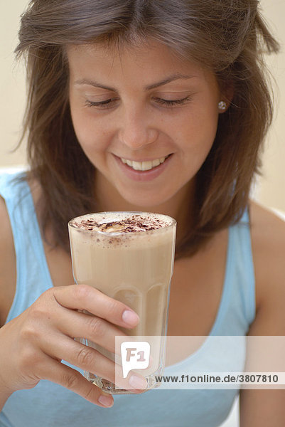 Junge Frau trinkt Milchkaffee Cappuccino aus einem Glas
