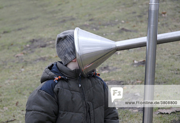 Little boy sticking his head into the funnel of an intercom in a playground