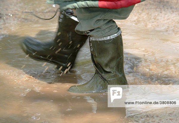 A child in rubber boots is splashing around in a puddle