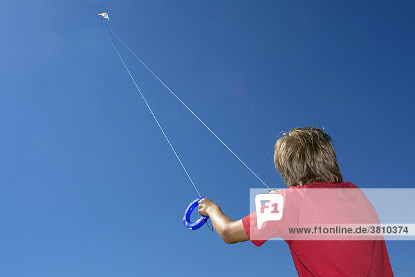 Junge lässt einen Lenkdrachen hoch am Himmel fliegen