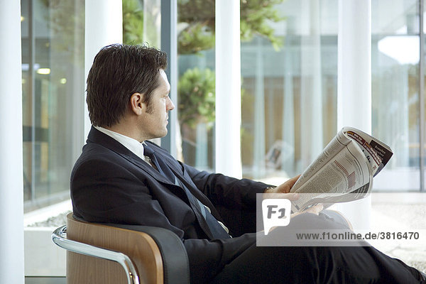 Mann sitzt in einem Sessel mit Zeitung in der Hand