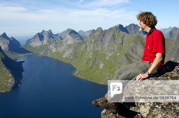 MR mountaineerer enjoys the grand view from summit Navaren on rough mountains with fjord Kjerkfjorden Moskenesoya Lofoten Norway