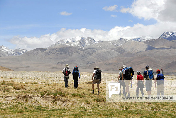 Trekking group passes wide river plain with snow capped mountains in the background near Lungchang Tibet China