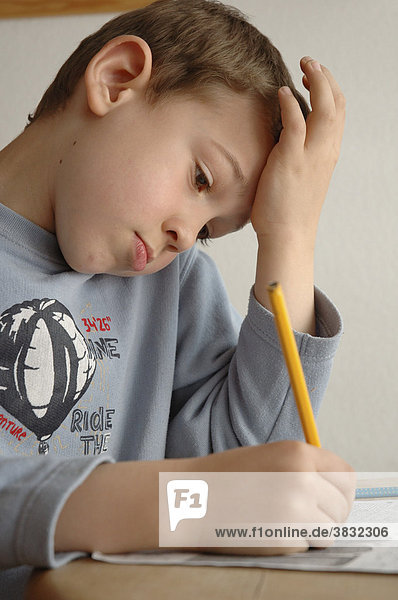 Junge in blauem Shirt sitzt am Tisch und arbeitet mit Papier und Bleistift