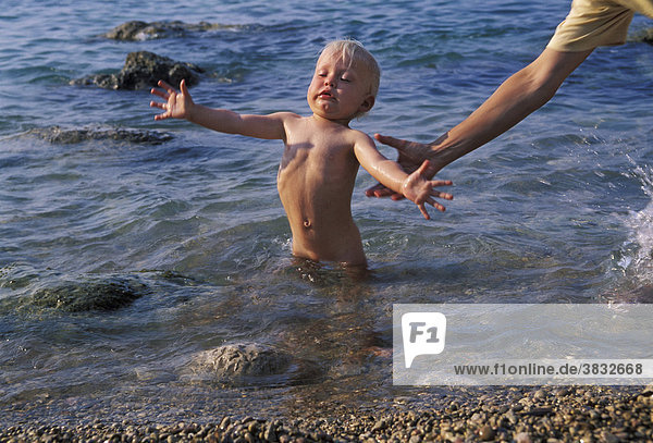 One-year-old standing in the water and falling over - hand holding him