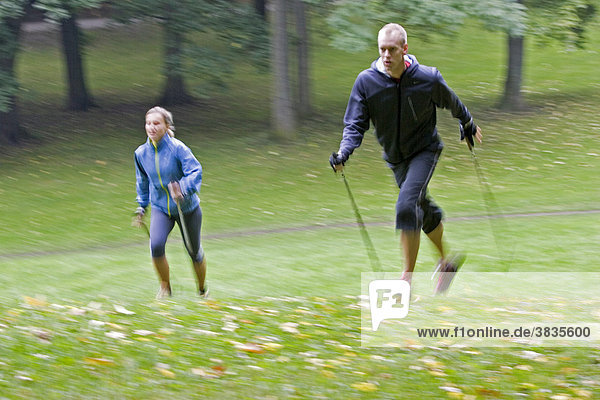 Zwei Nordic Walker mit Stöcke und sportliche Kleidung laufend auf einer grünen Wiese im Englichen Garten in München