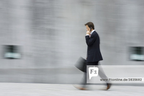 Mitzieher eines schnell laufenden Geschäftsmannes mit Aktentasche in der Hand vor einer hohen Betonwand in München