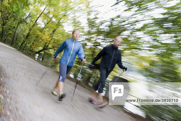 Unscharfe Frontansicht zweier Nordic Walker mit Stöcke und sportliche Kleidung auf einem Weg im Englischen Garten in München