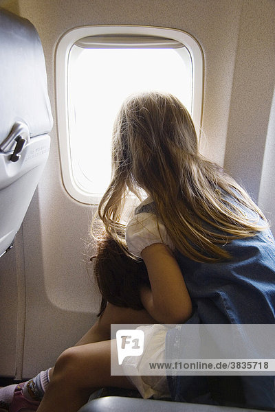 Kleines Mädchen mit Puppe schaut aus Flugzeugfenster