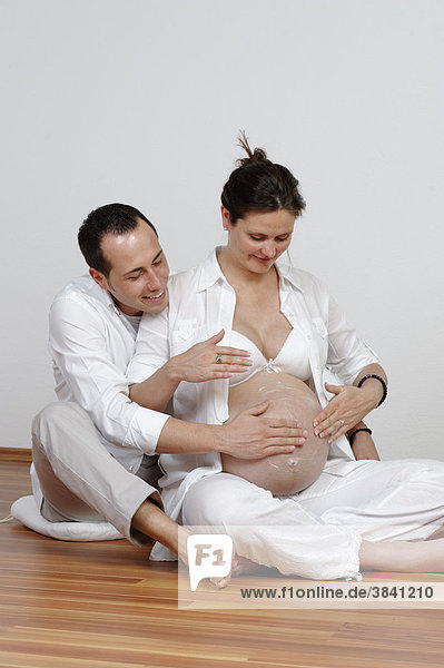 Schwangere Frau mit Kindsvater  der ihren Babybauch eincremt