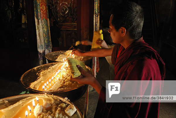 Pilgrim and Tibetan monks refilling the brass bow with yak butter  Samye Monastery  Tibet  China  Asia