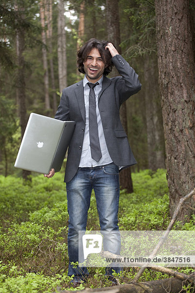 Young laughing businessman with laptop in a forest