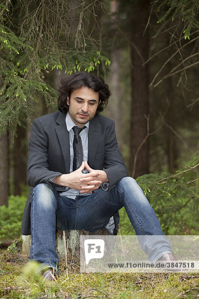 Young man sitting thoughtfully on a tree stump in a forest