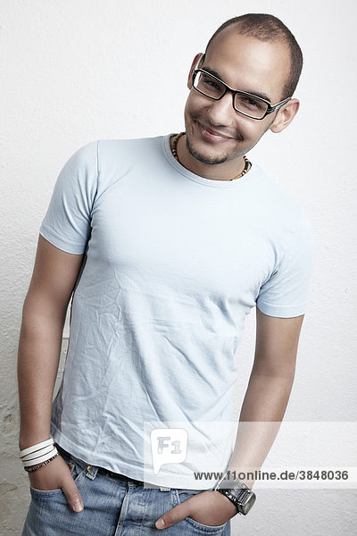 Young man with glasses  jeans and T-shirt smiles with his hands in his pockets