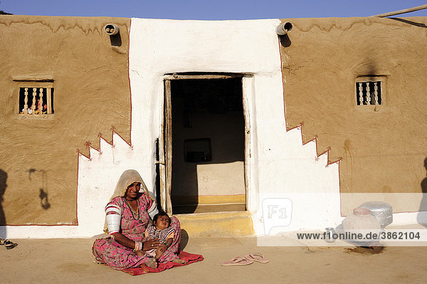 Eine Mutter mit ihrem Kind vor dem bemalten Eingang zu ihrem Wohnhaus  Wüste Thar  Rajasthan  Indien  Asien