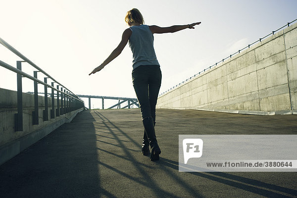 Teenagerin  die auf dem Schatten des Geländers auf dem Bürgersteig läuft  als ob sie auf dem Geländer selbst balanciert.