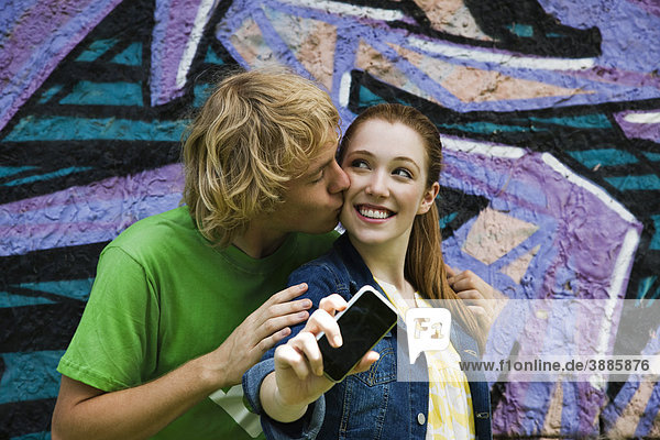 Junges Paar fotografiert sich mit dem Handy  Männchen küsst weibliche Wange