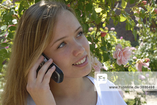 Mädchen in einem Rosengarten telefoniert mit einem Handy  Schweden  Skandinavien  Europa