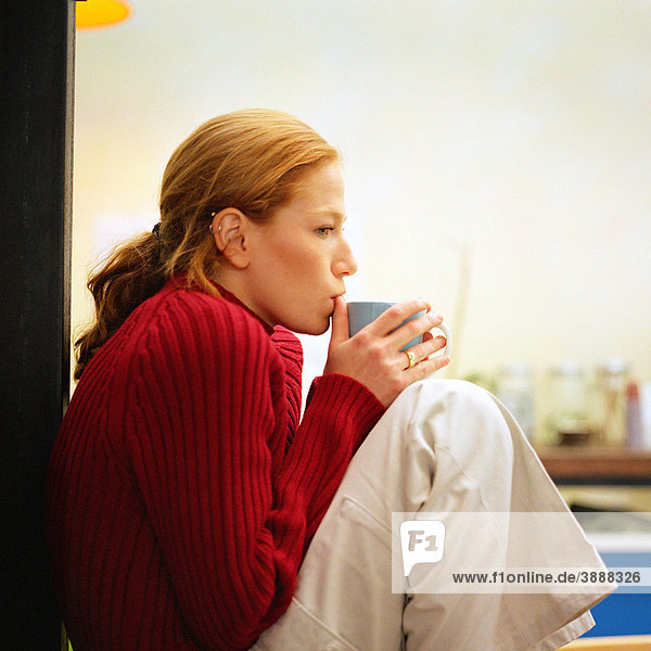 Junge Frau sitzend trinkend aus der Tasse  Seitenansicht