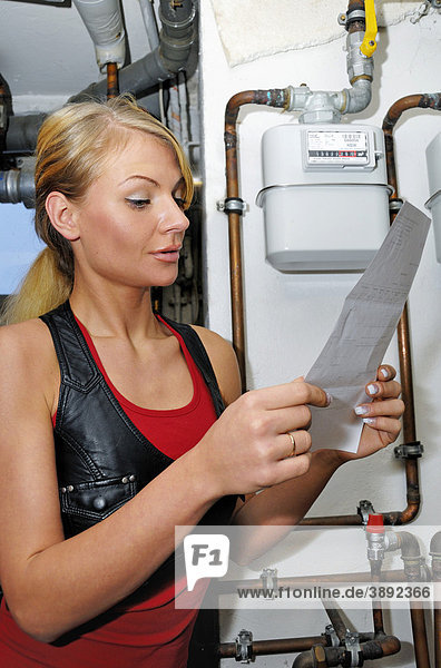 Young woman with heating cost bill  at the gas meter
