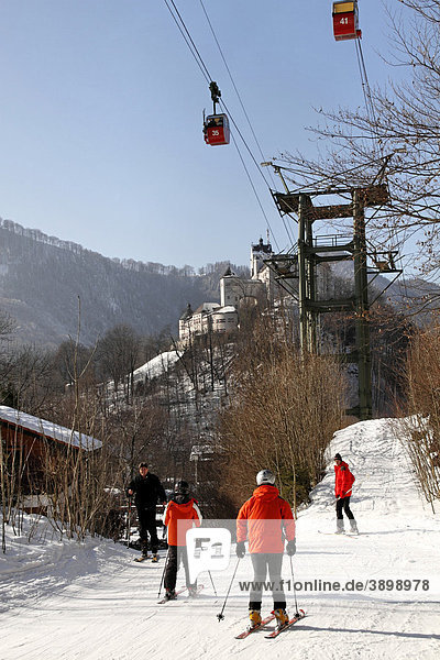 Skiers on pathway with cable cars overhead and Aschau Castle in the back  Upper Bavaria  Germany  Europe
