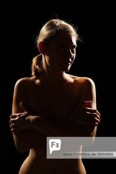 Junge Frau bedeckt den nackten Oberkörper mit verschränkten Armen  Gegenlicht