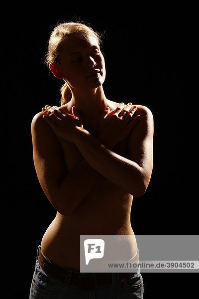 Young woman covering her naked torso with her folded arms  backlight