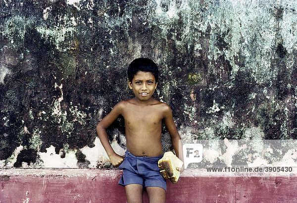 Kleiner singhalesischer Junge mit nacktem Oberkörper und Shorts hält ein Stück Brot  Porträt  Sri Lanka  Ceylon  Südasien  Asien
