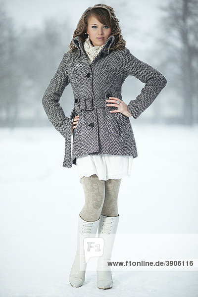Jungen Frau im Schnee  trägt Mantel  Strumpfhose und Stiefel