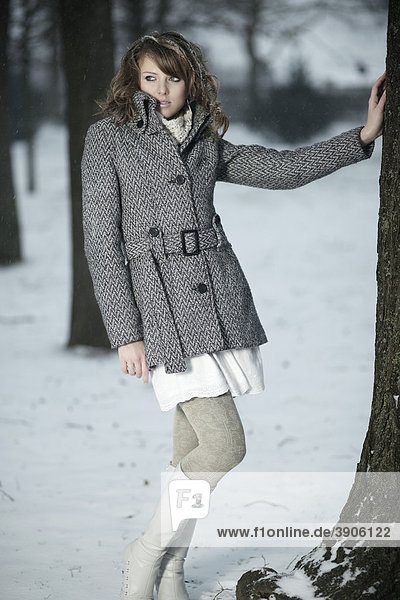 Junge Frau im Schnee  ihre Hand an einen Baumstamm haltend