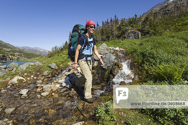 Junge Frau überquert Bach  kleiner Wasserfall  Wandern  Wanderin mit Rucksack  historischer Chilkoot Pass  Chilkoot Trail  alpine Tundra  Yukon Territorium  British Columbia  BC  Kanada