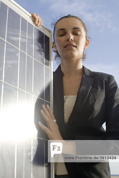 Junge Frau genießt die Sonnenkraft und hält dabei ein Solarmodul