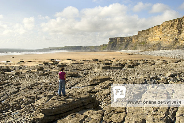 Frau auf Stein schaut auf Strand und Klippen  Küste  Nash Point  Glamorgan Heritage Coast  Südwales  Wales  Großbritannien  Europa