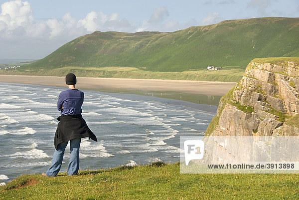 Woman standing on a cliff  overlooking waves and a beach  Rhossili Beach  Gower Peninsula  Wales  United Kingdom  Europe