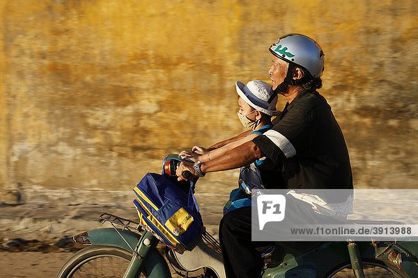 Ein vietnamesischer Vater mit seinem Sohn auf dem Motorroller mit Rucksack in Hoi An  Vietnam  Südostasien