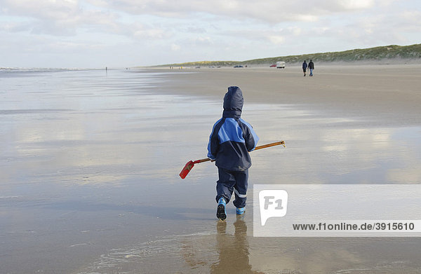Kleiner Junge  2 Jahre  läuft mit einer Schaufel über den Nordseestrand  Vejers Strand  Jütland  Dänemark  Europa