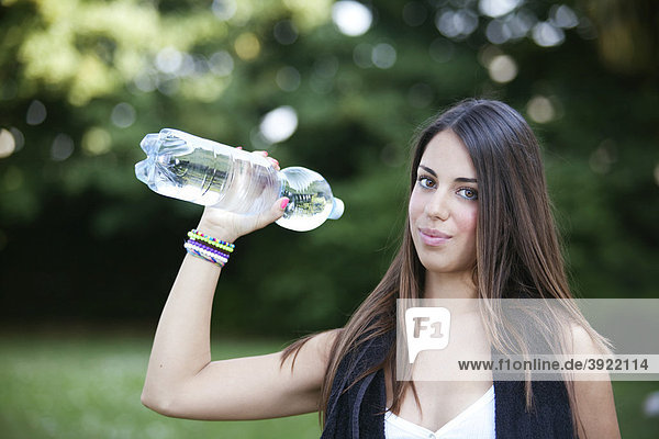 Junge Frau hält sich fit indem sie mit einer Flasche Wasser trainiert
