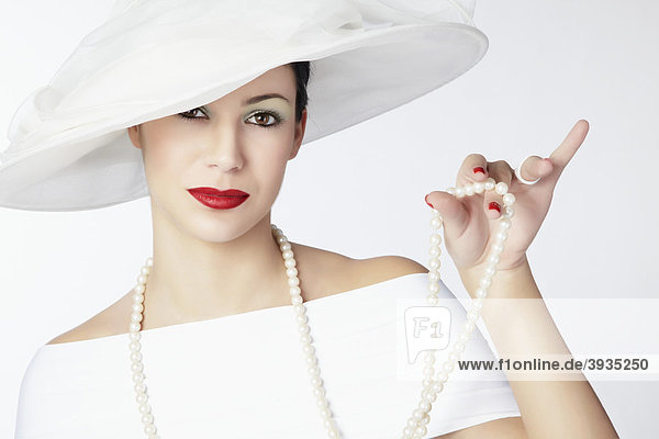 Portrait einer jungen Frau mit weißem Sommerhut  weißem Kleid und Perlenkette in der Hand