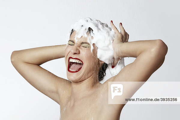 Cheerful young woman in the shower with foam in her hair