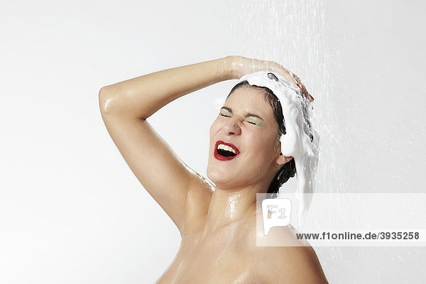 Fröhliche junge Frau mit Schaum in ihrem Haar beim Duschen
