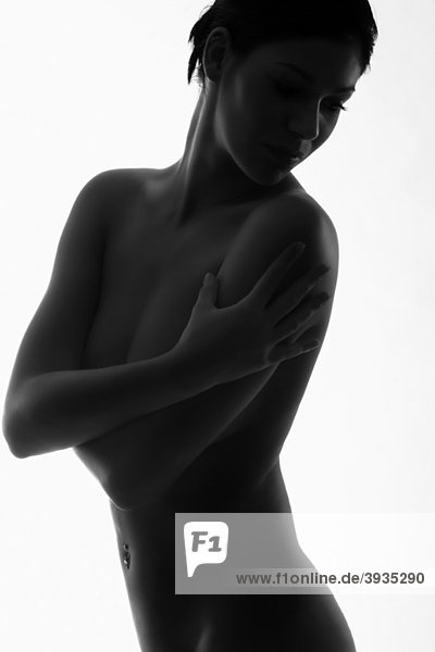Silhouette einer nackt dastehenden jungen Frau mit Blick über ihre Schulter