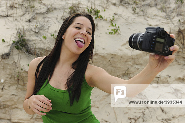 Frau mit digitaler Spiegelreflexkamera macht ein Selbstportrait am Strand