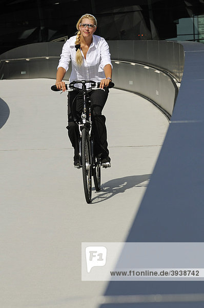Young woman riding a bicycle in front of BMW Welt  Munich  Bavaria  Germany  Europe