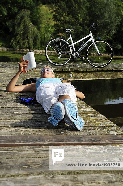 Young woman reading a book beside Olympic Lake  Munich  Bavaria  Germany  Europe